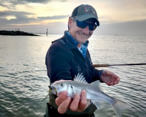 Flyfisherman at dawn on the dorset coast with sun behind clouds behind, fisherman in cap with rod holding a sea bass