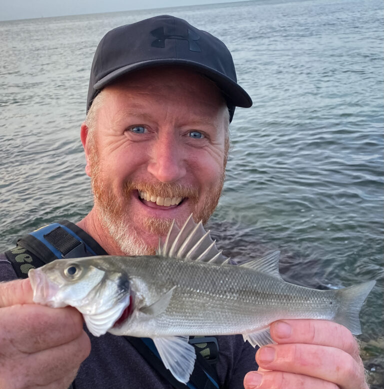 smiling flyfishing angler in cap with bass held in front