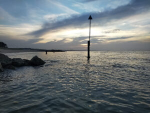 Dawn on the Dorset coast sea groyne and marker with sun rising over the sea and clouds behind