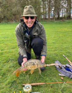 Smiling flyfisherman holding Mirror Carp with flyrod in foreground