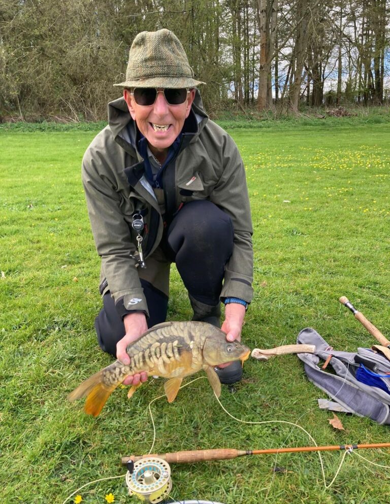 Smiling flyfisherman holding Mirror Carp with flyrod in foreground