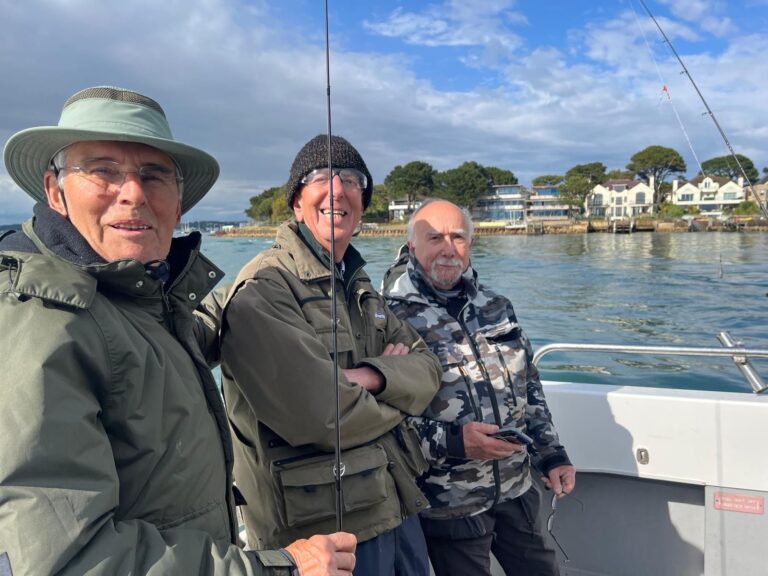 three fishermen at the entrance to Poole Harbour, on boat with houses in background