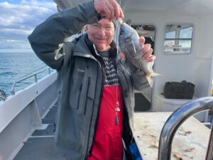 Man holding a Sea Bream fish on a boat with sea in background