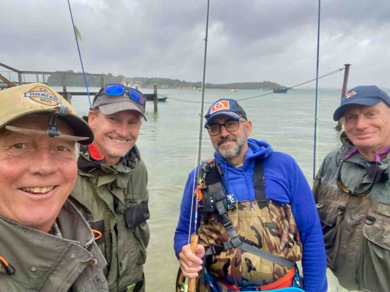 4 fly anglers holding flyfishing rods with harbour and water in background